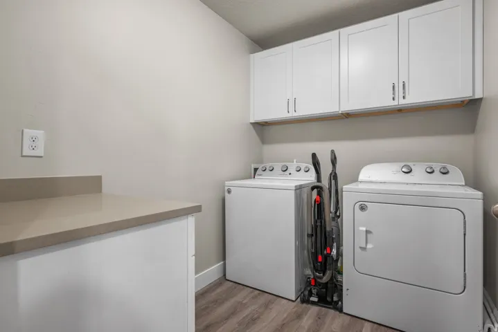 Laundry area featuring wood-finish flooring, white shaker-style cabinetry, a light-toned countertop, a light gray wall finish, and a white baseboard trim