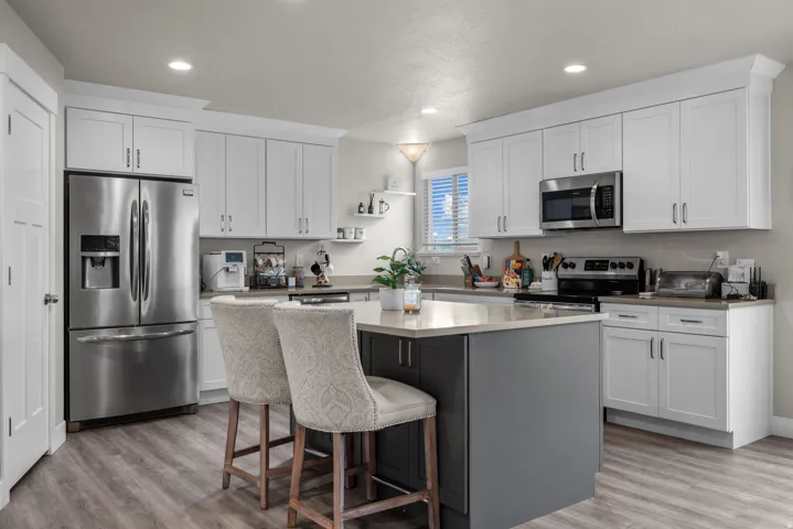 Modern kitchen featuring white shaker-style cabinetry, a contrasting island with seating, stainless steel appliances, light gray countertops, and wood-finish flooring