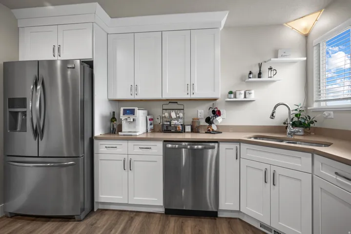 Contemporary kitchen featuring white cabinetry, a stainless steel refrigerator, stainless steel dishwasher, light-toned countertops, and wood-finish flooring