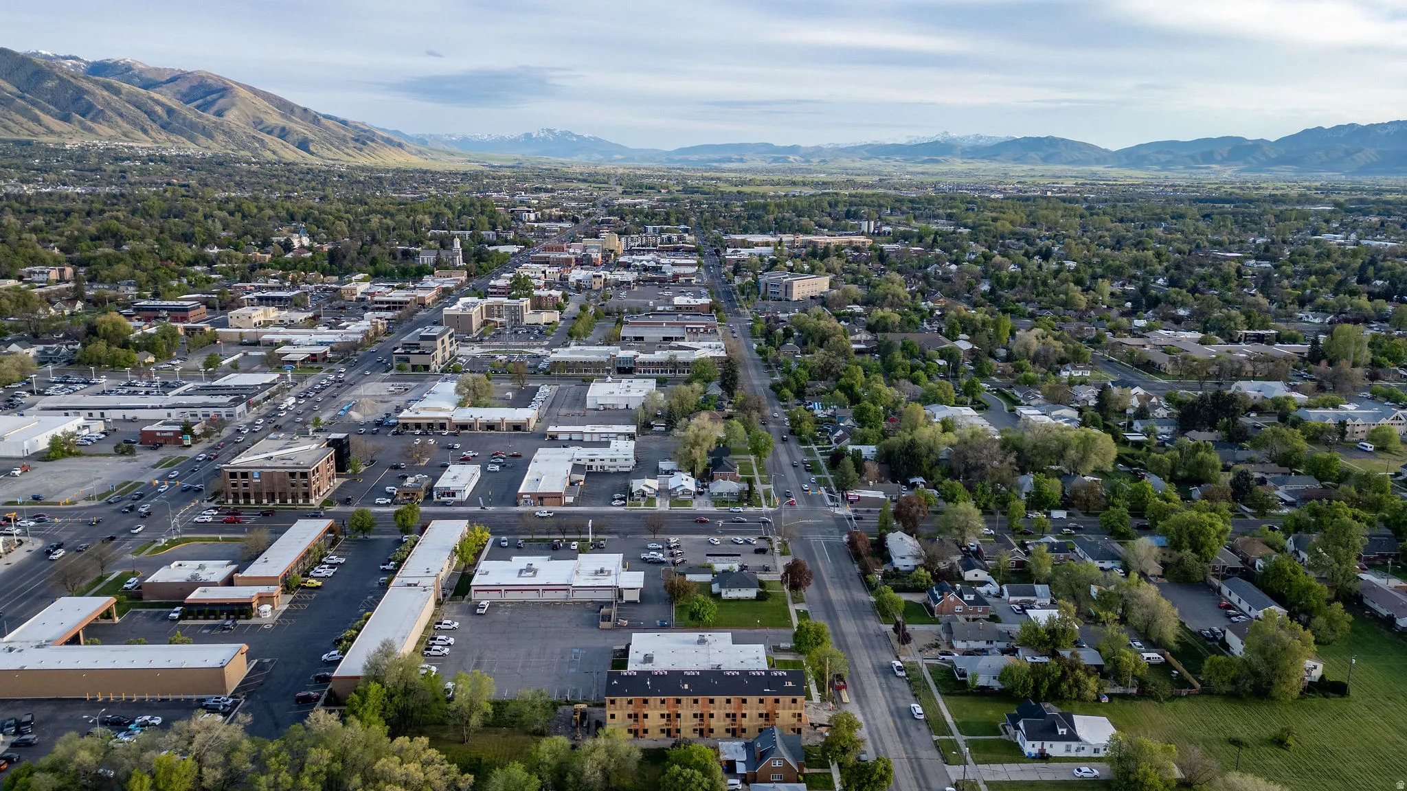 Expansive aerial perspective showcasing a developed urban area with surrounding green spaces and distant mountain ranges