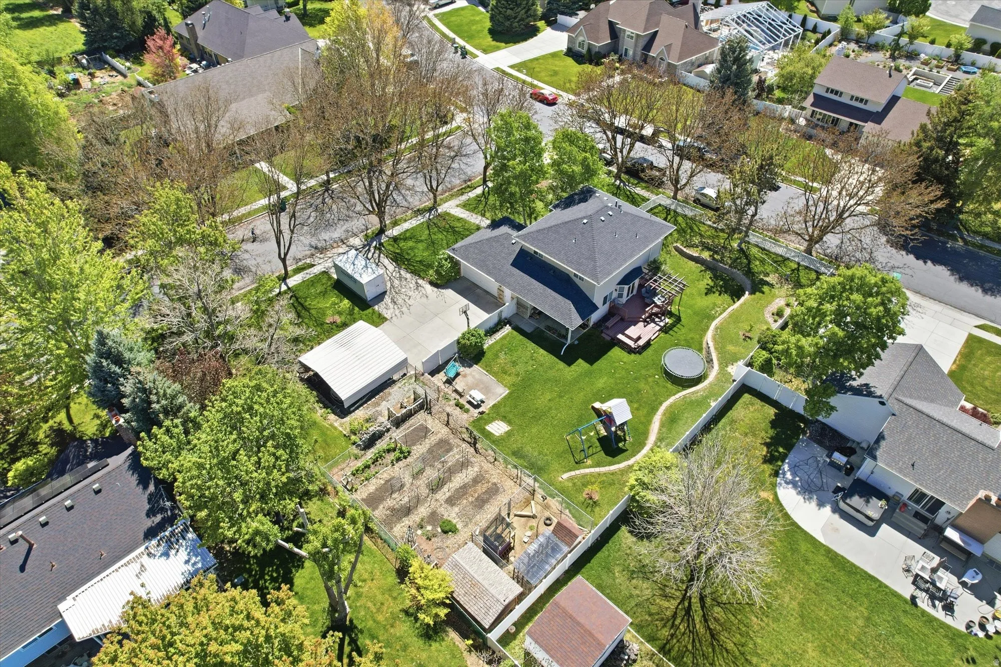 Expansive property featuring a two-story residence with a dark shingle roof, a large backyard with a manicured lawn, a terraced garden area, a concrete driveway, and mature landscaping