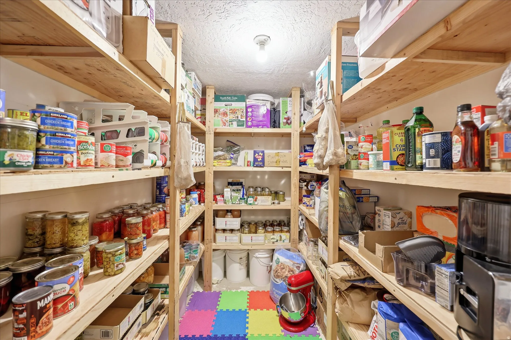Spacious pantry featuring extensive wood shelving, bright overhead lighting, textured ceiling, and durable flooring