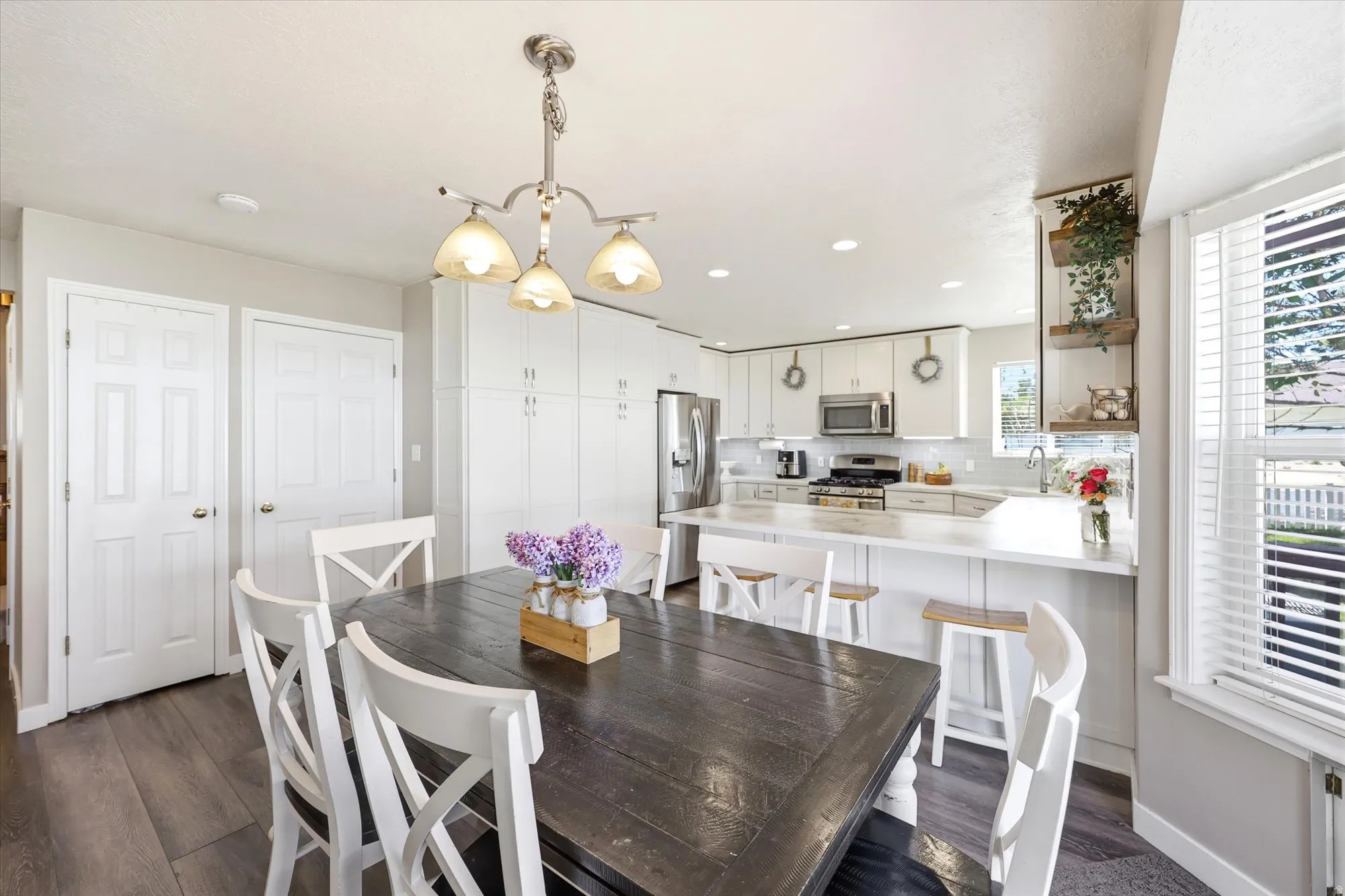 Open-concept kitchen and dining area featuring wood-finish flooring, white cabinetry, stainless steel appliances, a kitchen island with seating, and a window with blinds