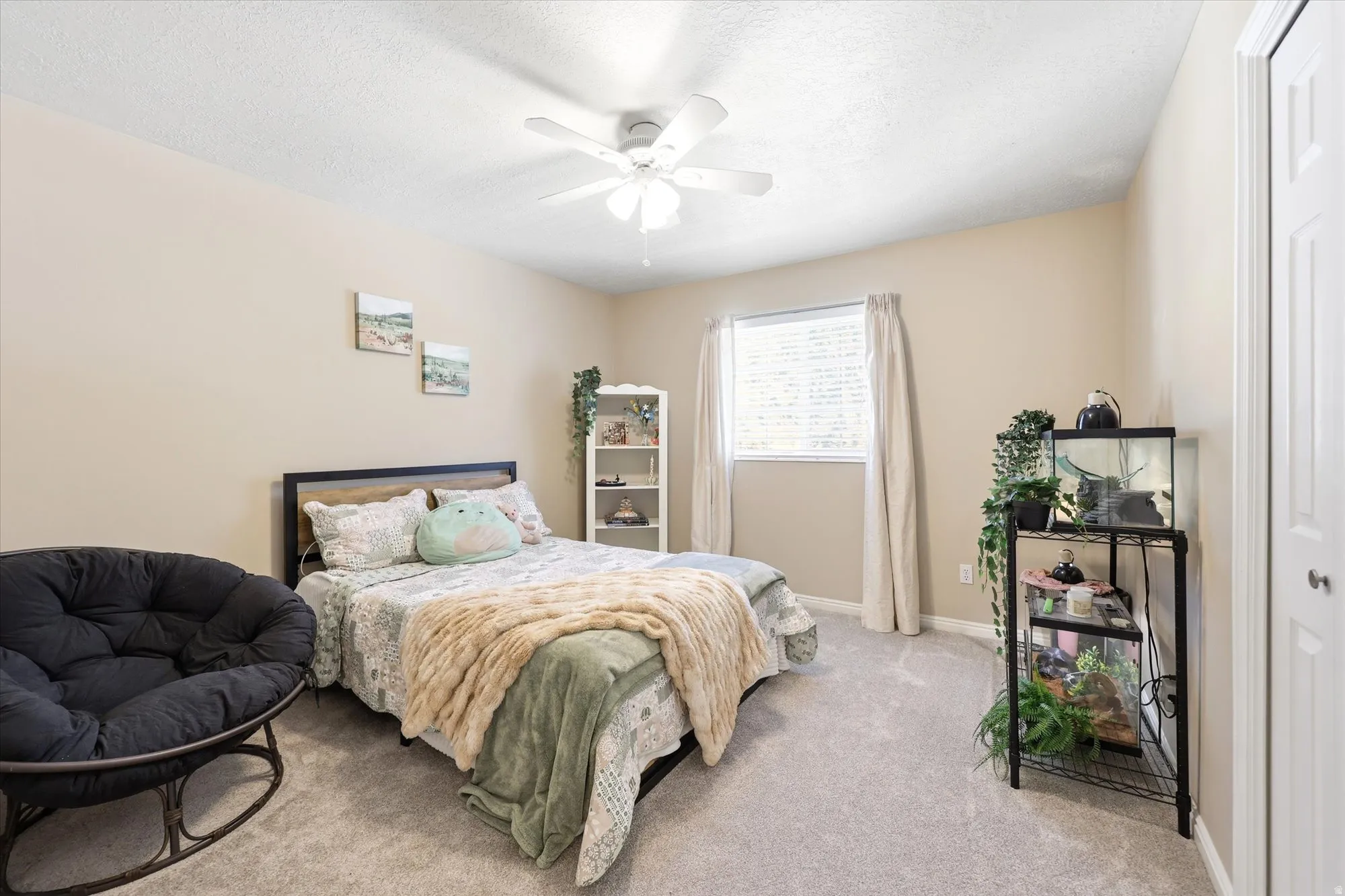 Bedroom featuring light beige walls, gray carpet flooring, a white ceiling fan, and a single window with blinds and drapes