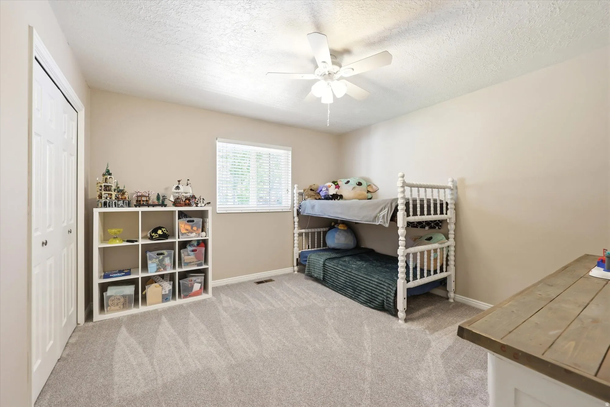 Spacious room featuring neutral paint, gray patterned carpeting, a white bi-fold closet, a window with horizontal blinds, and a ceiling fan with integrated lighting