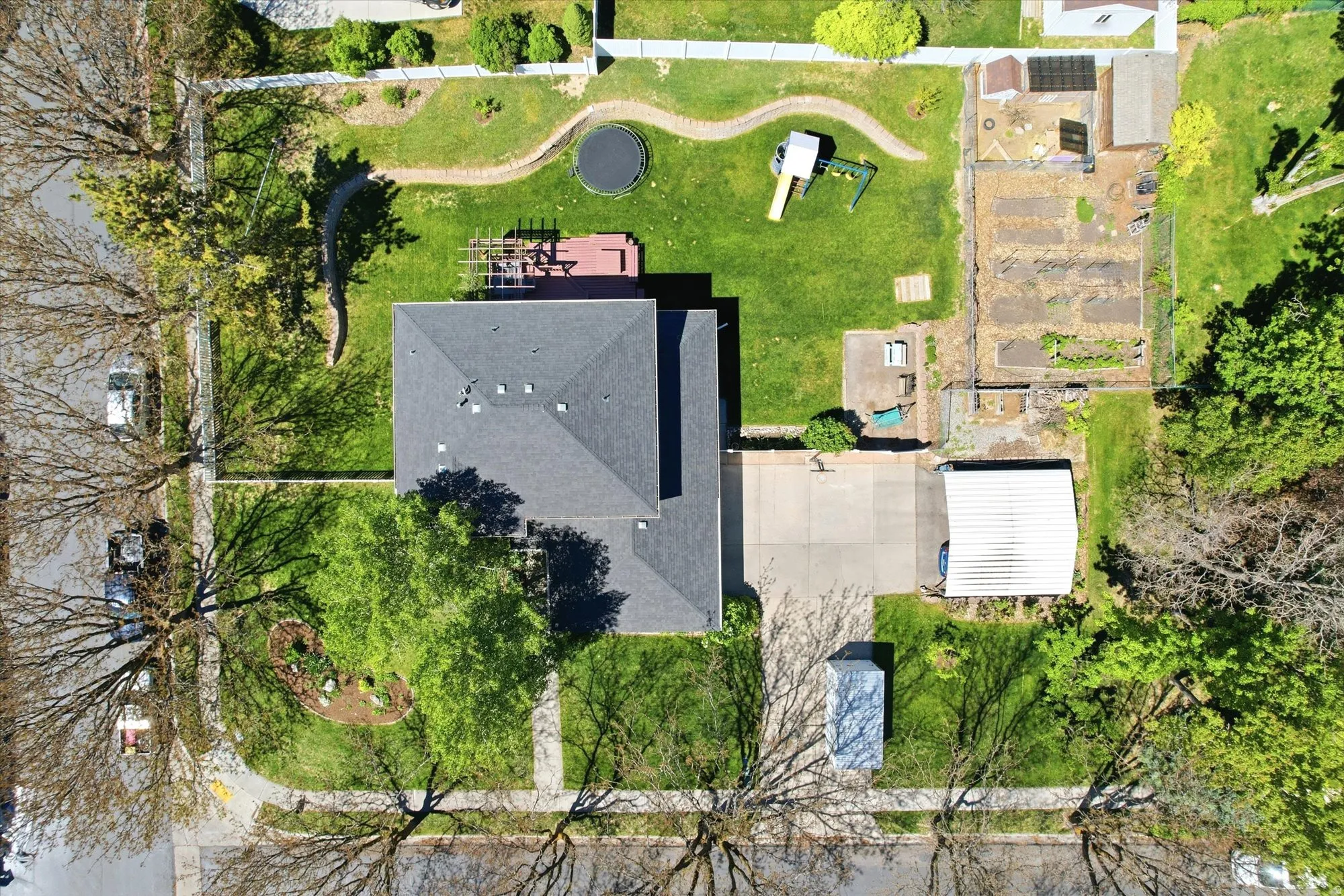 Property featuring a grey shingle roof, expansive green lawn, concrete driveway, and a fenced garden area