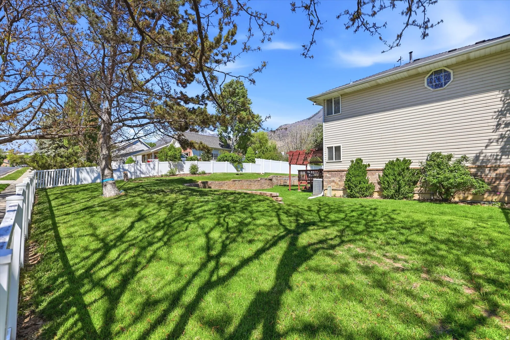 Expansive lawn area featuring a picket fence, mature trees, and a mountain backdrop