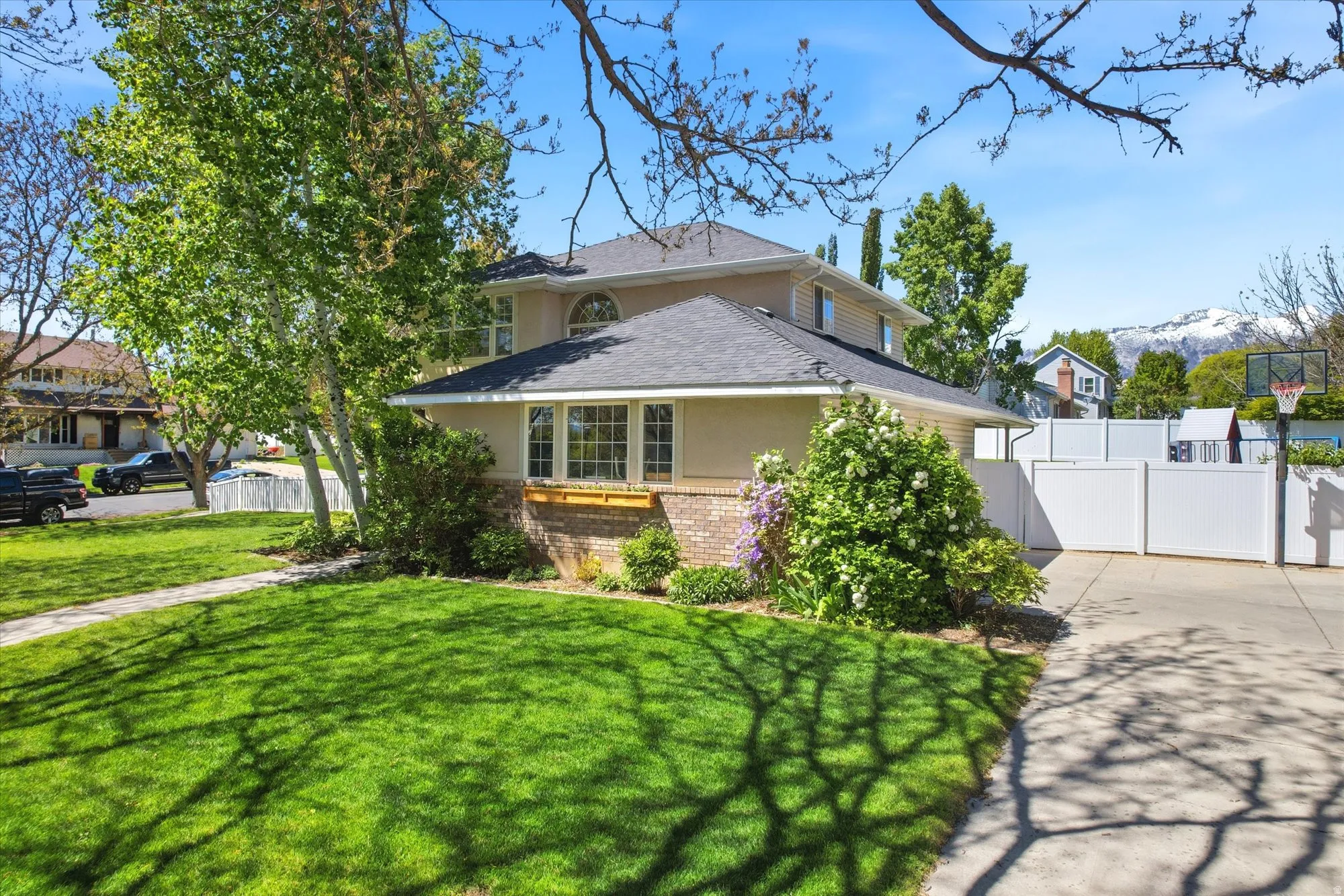 Traditional-style residence featuring a stucco and brick exterior, a manicured lawn, mature trees, and a paved driveway