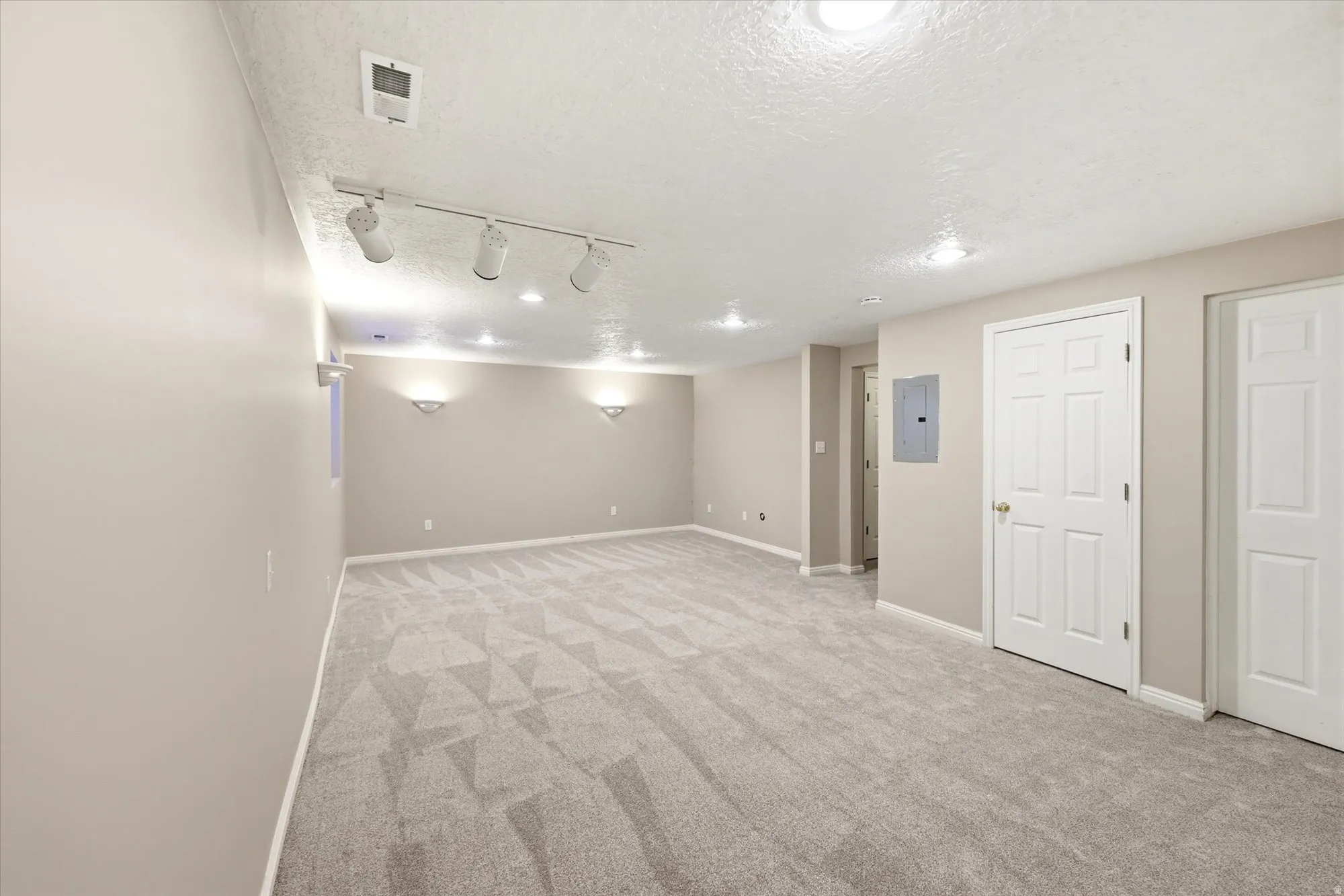 Spacious room featuring neutral-toned walls, patterned carpeting, recessed lighting, and track lighting