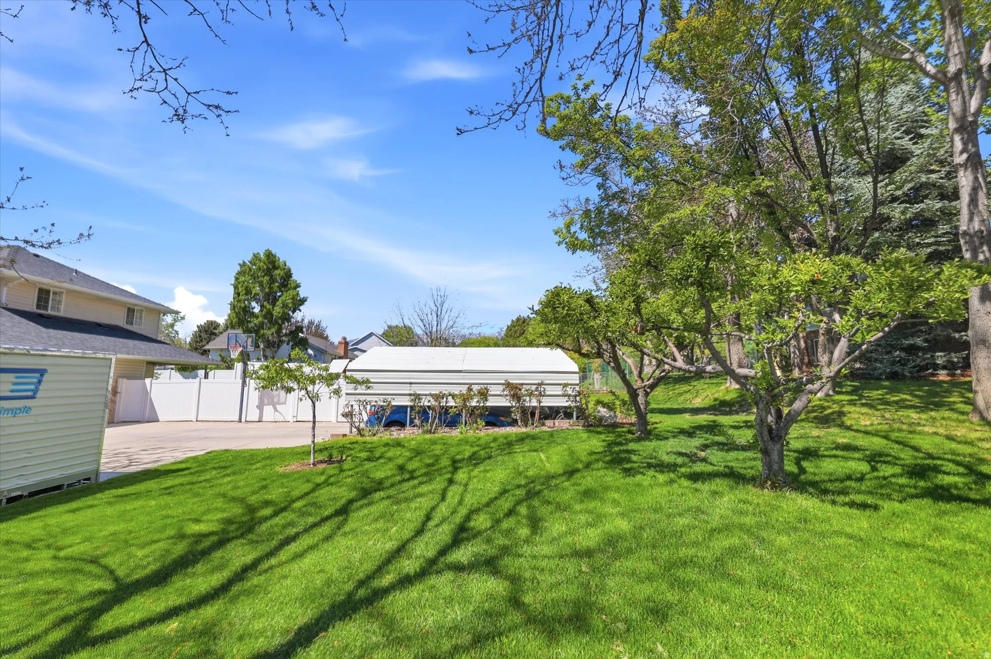 Expansive grassy yard with mature trees and a white privacy fence