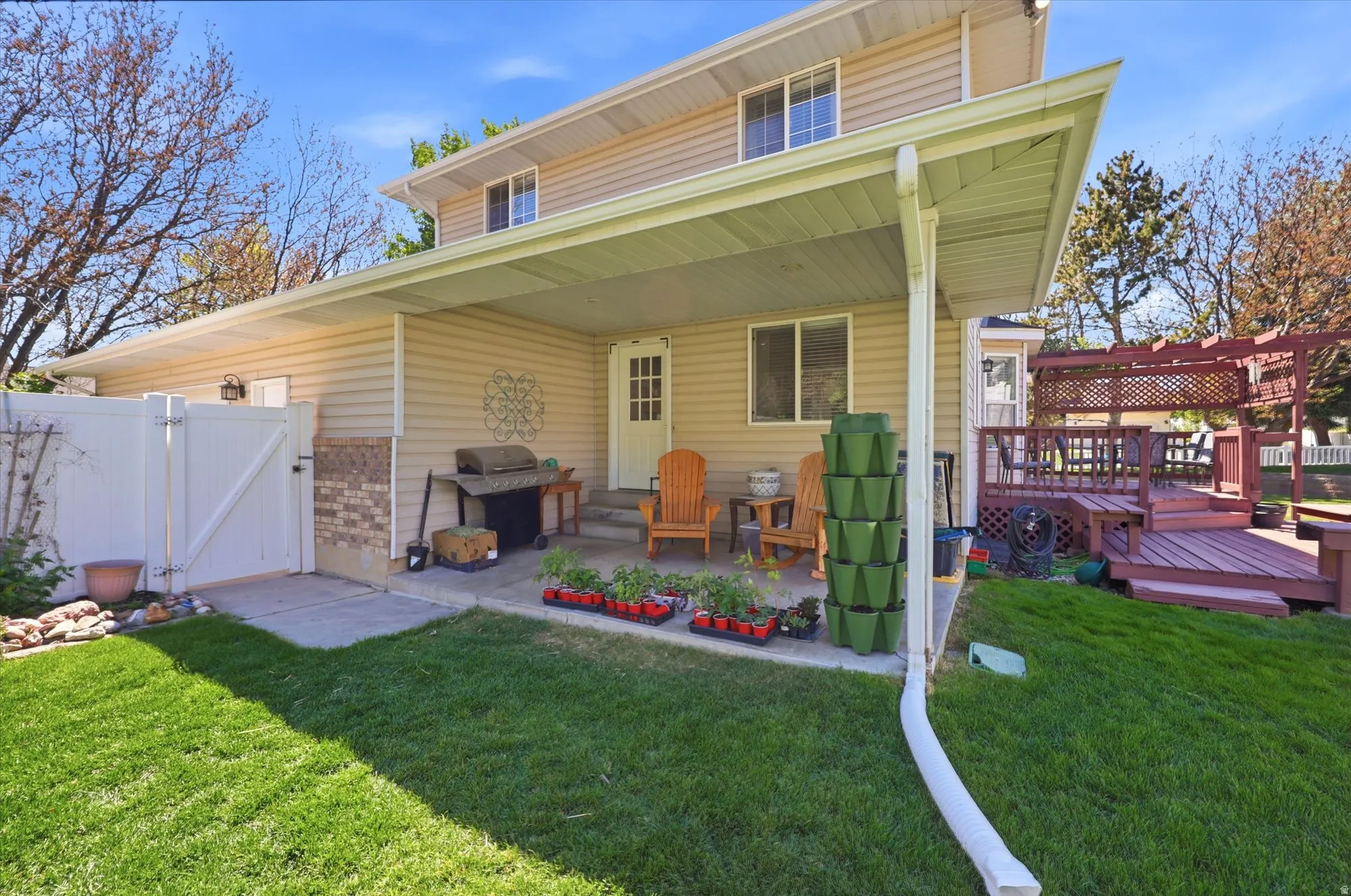 Rear exterior featuring a covered patio with a concrete slab, a multi-level wood deck with a pergola, a white vinyl privacy fence, and a manicured lawn