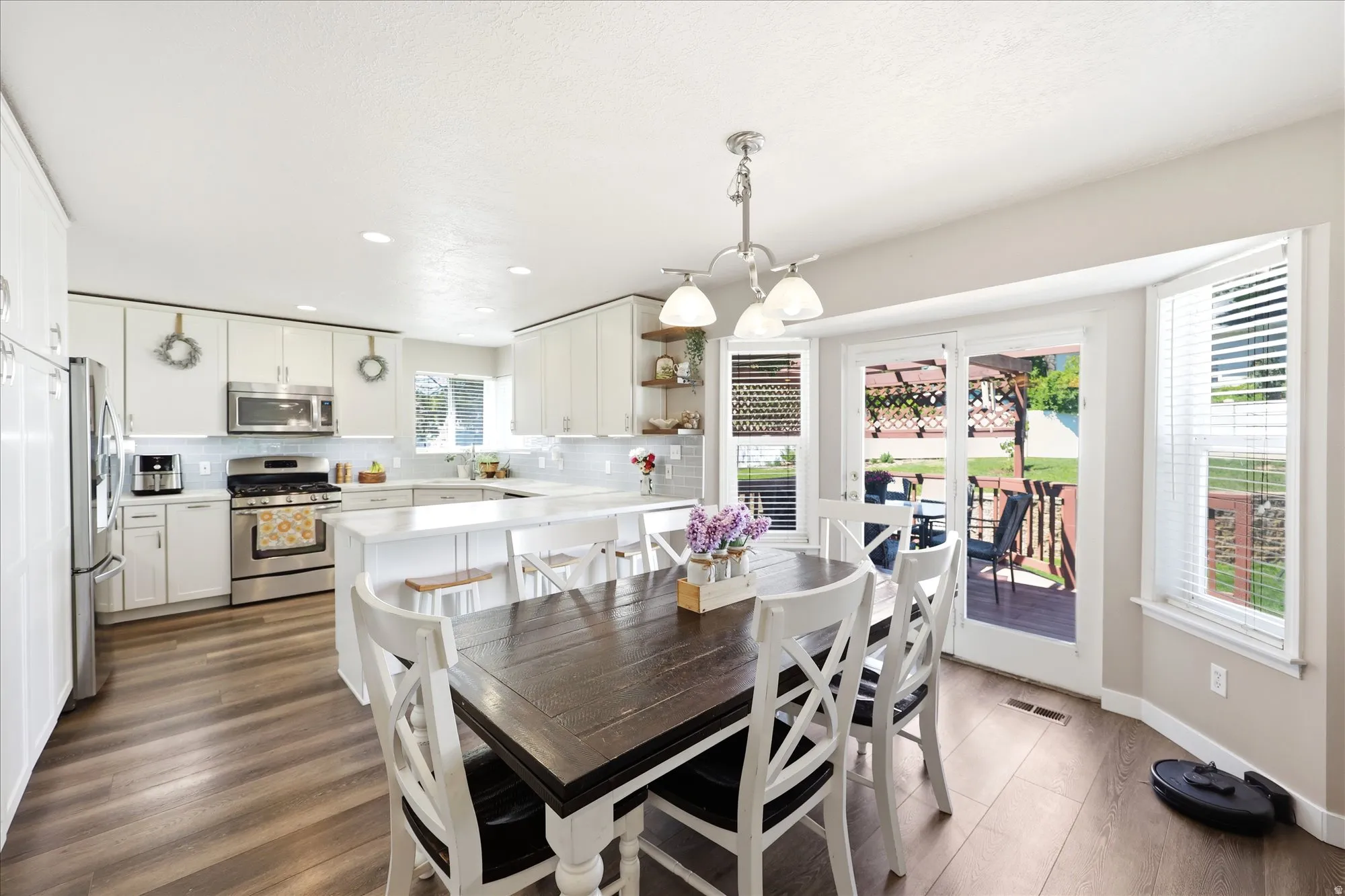 Kitchen and dining area featuring wood-finish flooring, white cabinetry, stainless steel appliances, and a sliding glass door leading to an outdoor deck