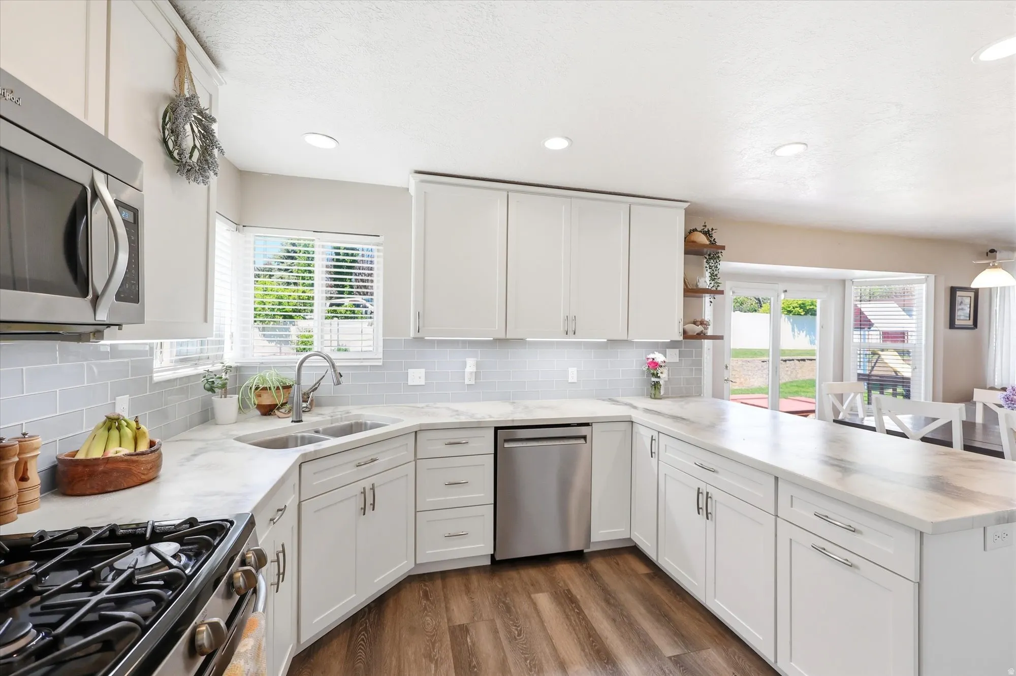 Spacious kitchen featuring white cabinetry, light gray subway tile backsplash, stainless steel appliances, wood-finish flooring, and recessed lighting
