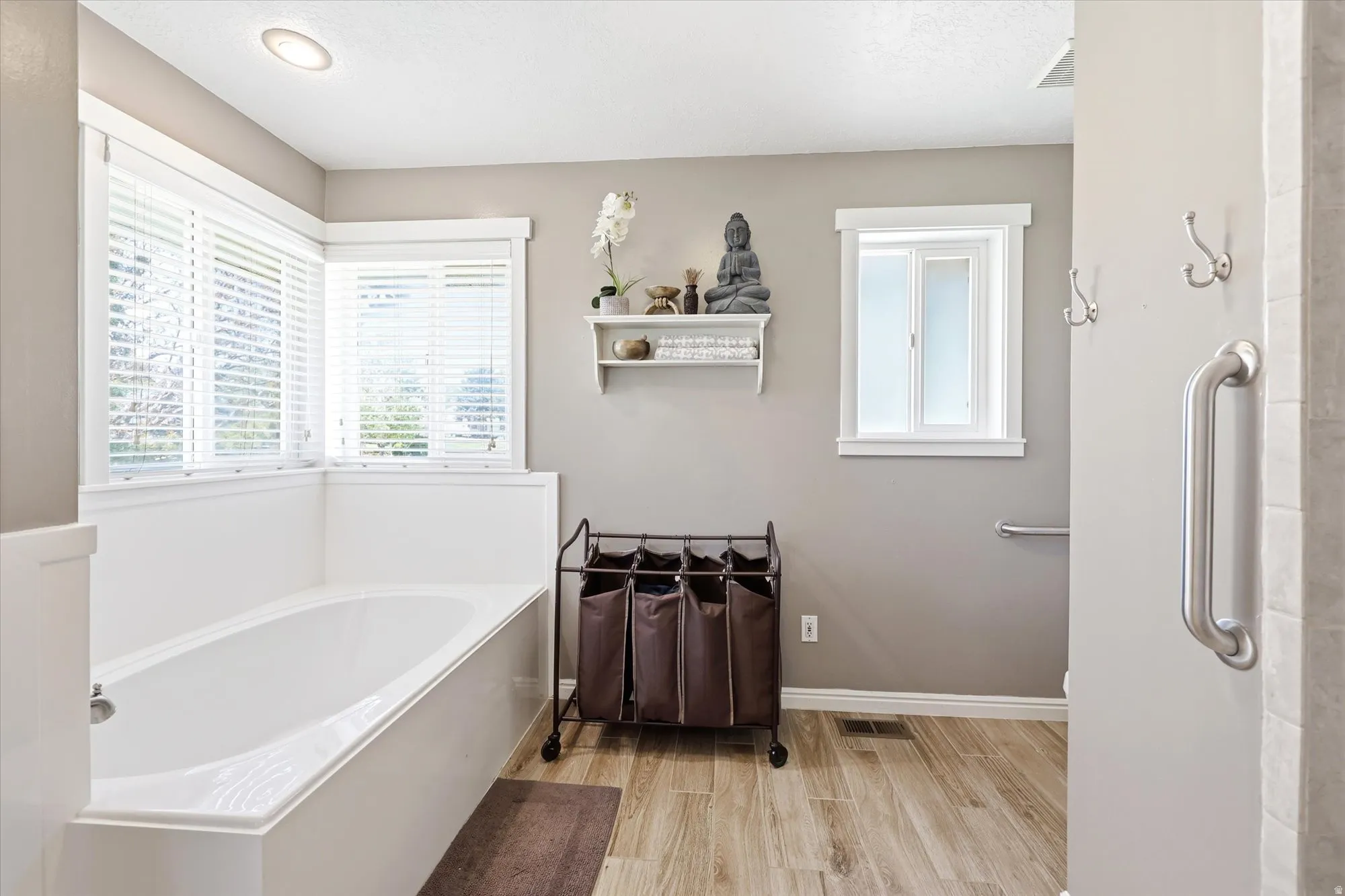 Soaking tub with white paneling situated beneath corner windows with blinds