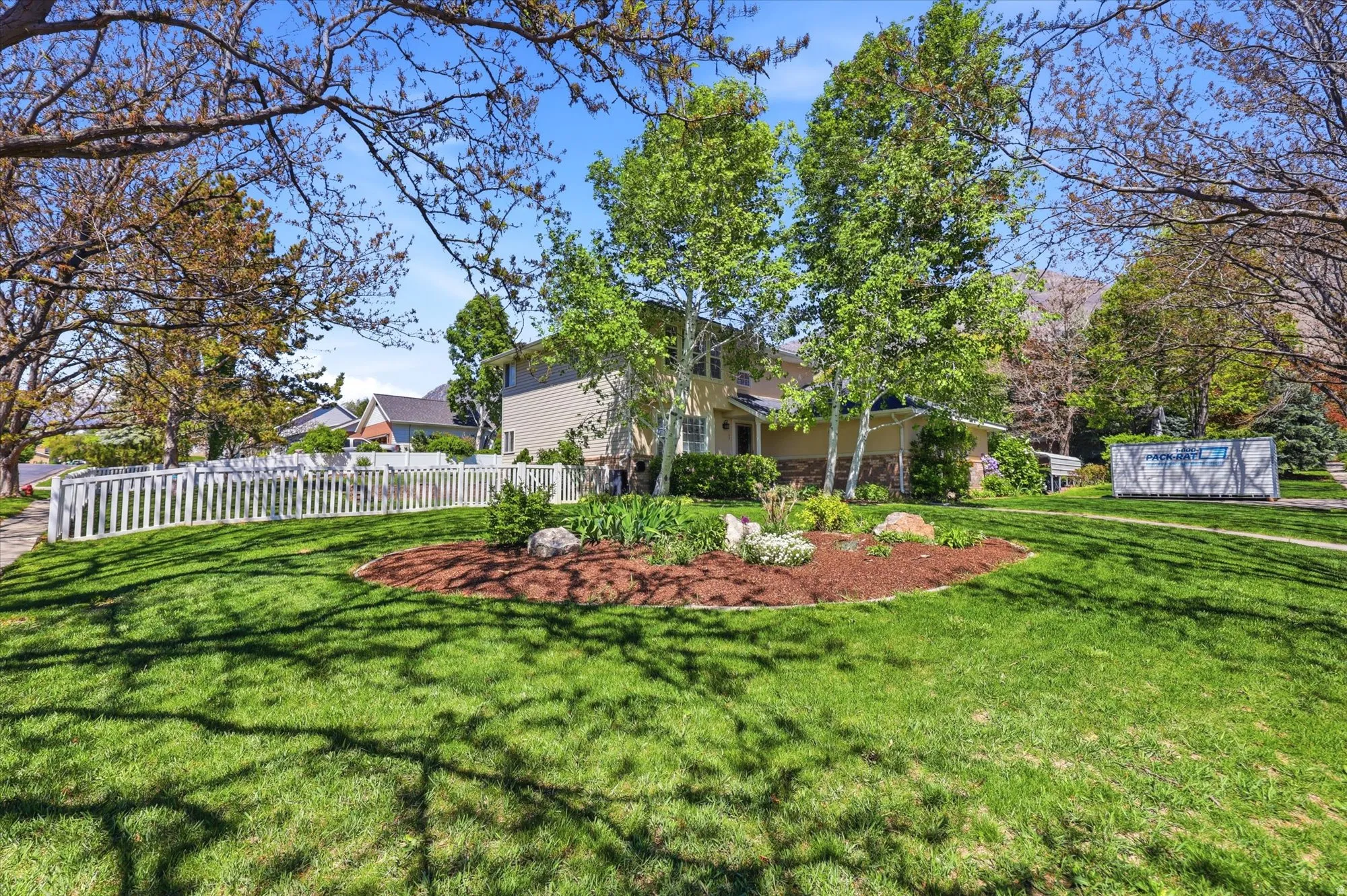 Expansive front lawn with mature trees and a white picket fence
