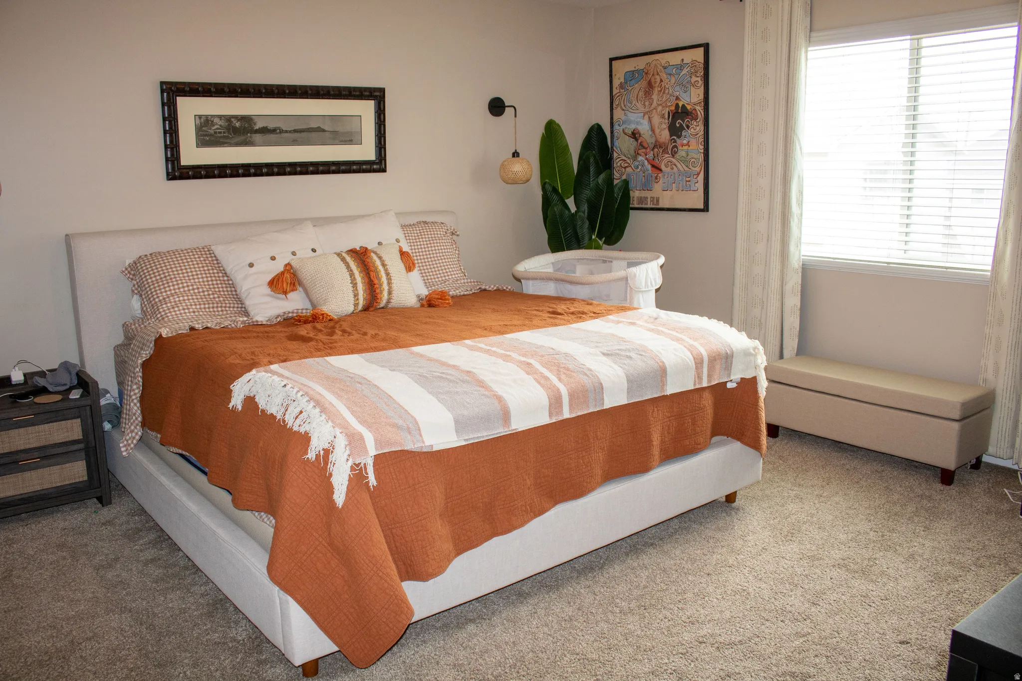 Carpeted bedroom featuring a window with blinds, a wall-mounted light fixture, and a built-in wall picture frame