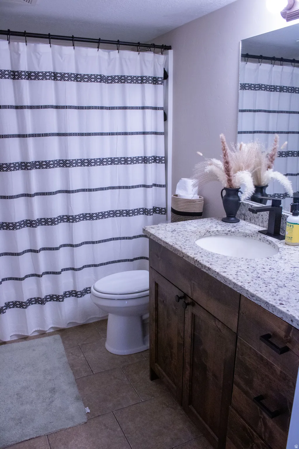 Bathroom featuring a wood-finish vanity with an integrated sink and granite-patterned countertop, ceramic tile flooring, and a white toilet