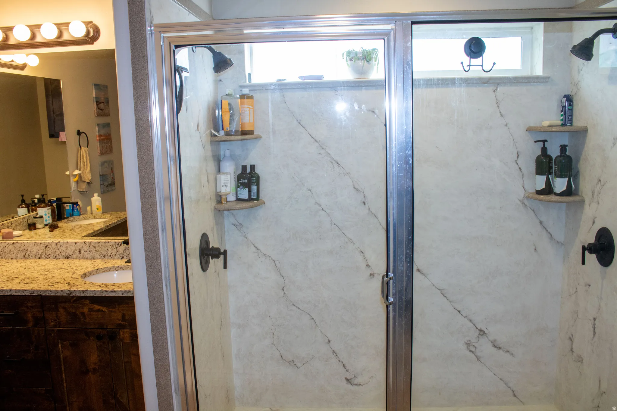 Walk-in shower with clear glass enclosure and light-toned, veined wall surrounds