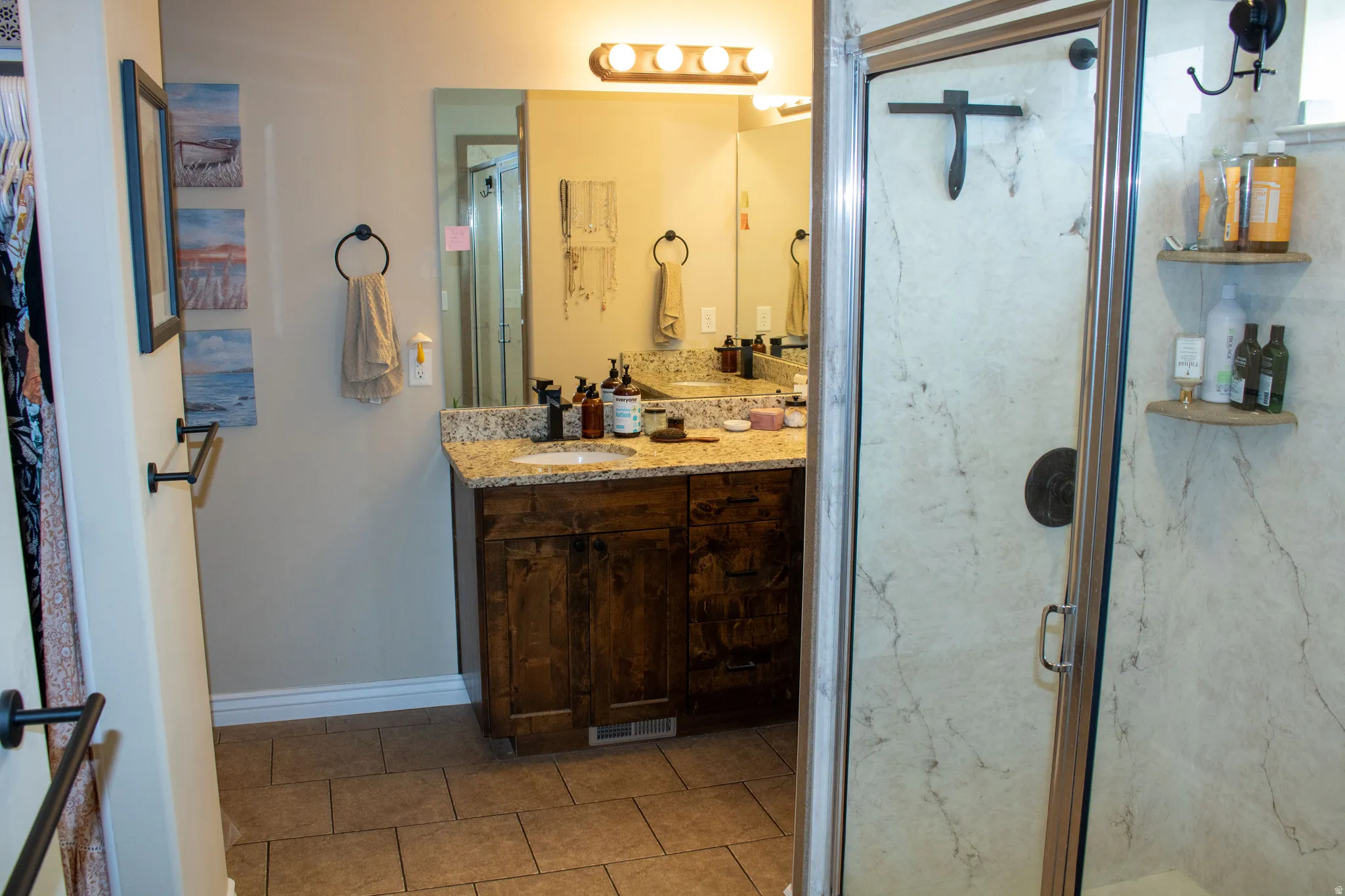 Bathroom featuring a glass-enclosed shower with a dark bronze shower fixture, a wood-finish vanity cabinet, a light-toned granite-style countertop, and a single basin sink
