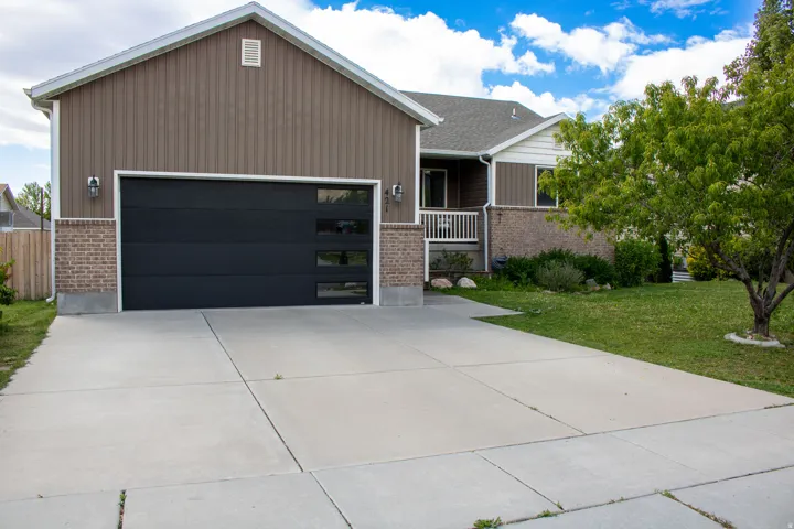 Contemporary exterior featuring a modern black garage door with frosted window panels, brown vertical siding, and a brick facade