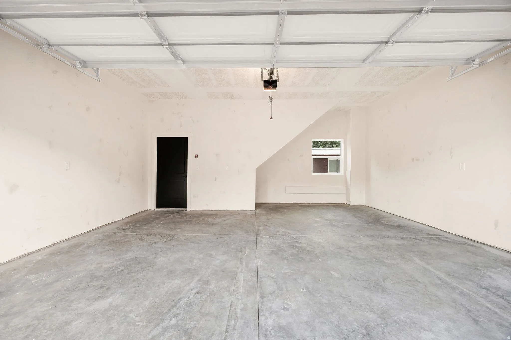 Spacious garage with concrete flooring, light-toned walls, and overhead garage door track system