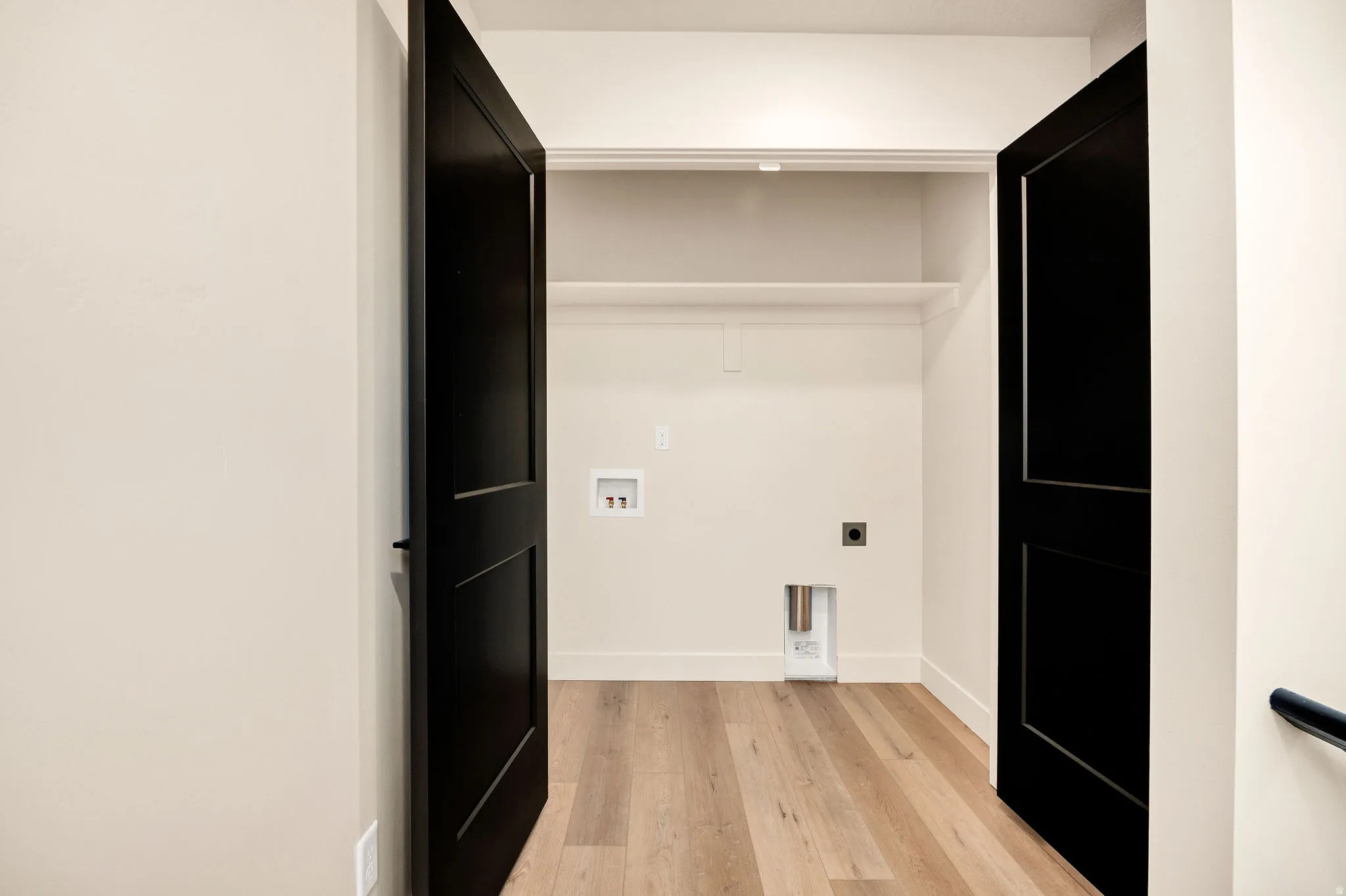 Sleek walk-in closet featuring black panel doors, white shelving with integrated lighting, wood-finish flooring, and electrical outlets for convenience