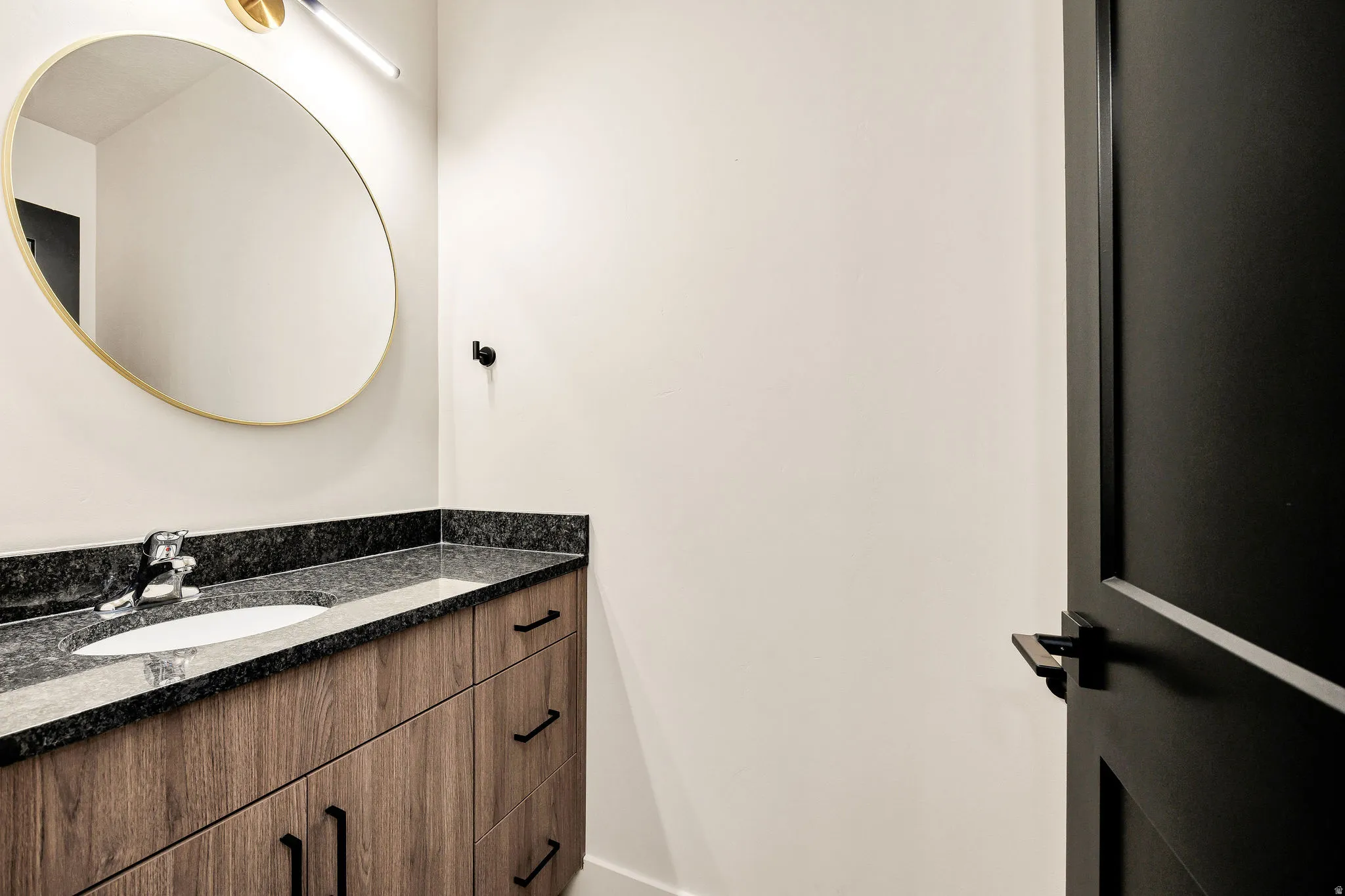 Contemporary vanity featuring wood-finish cabinetry, a dark granite countertop, and an undermount sink with a chrome faucet