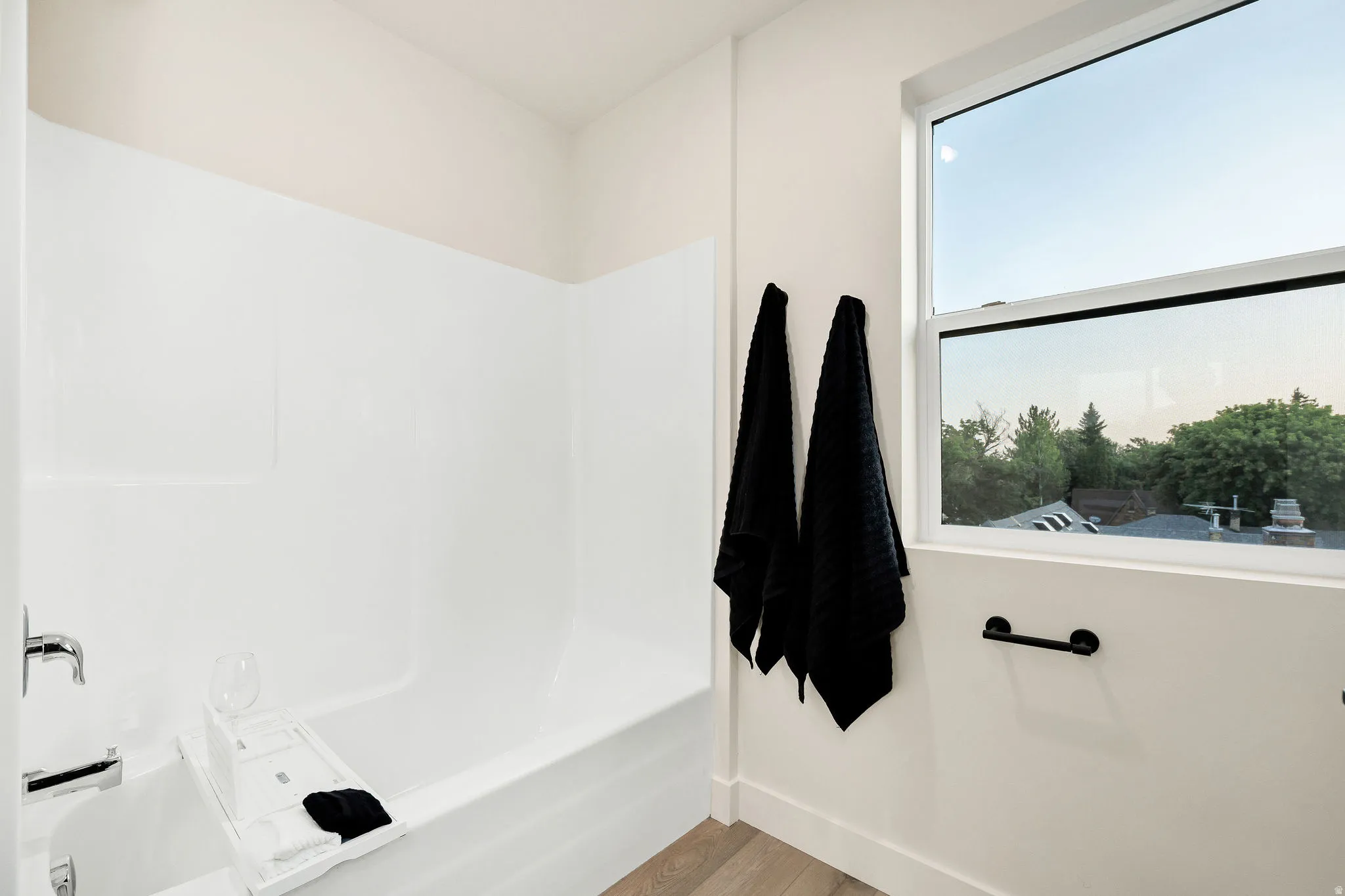 Bathroom featuring a white tub and shower surround, chrome fixtures, a modern window, and wood-finish flooring