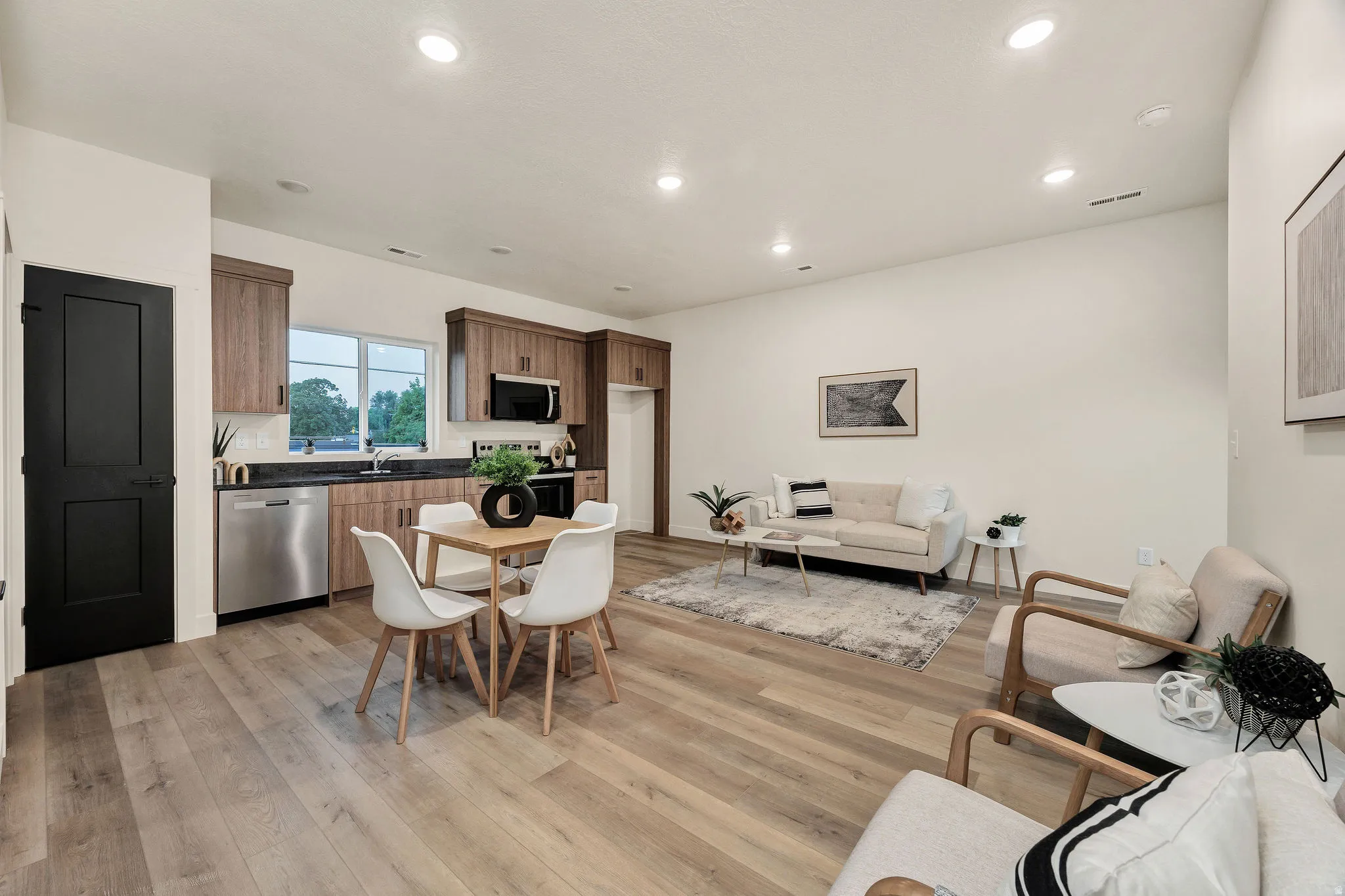 Open-concept living area featuring wood-finish flooring, recessed lighting, and a kitchen with wood cabinetry, stainless steel appliances, and a dark stone countertop