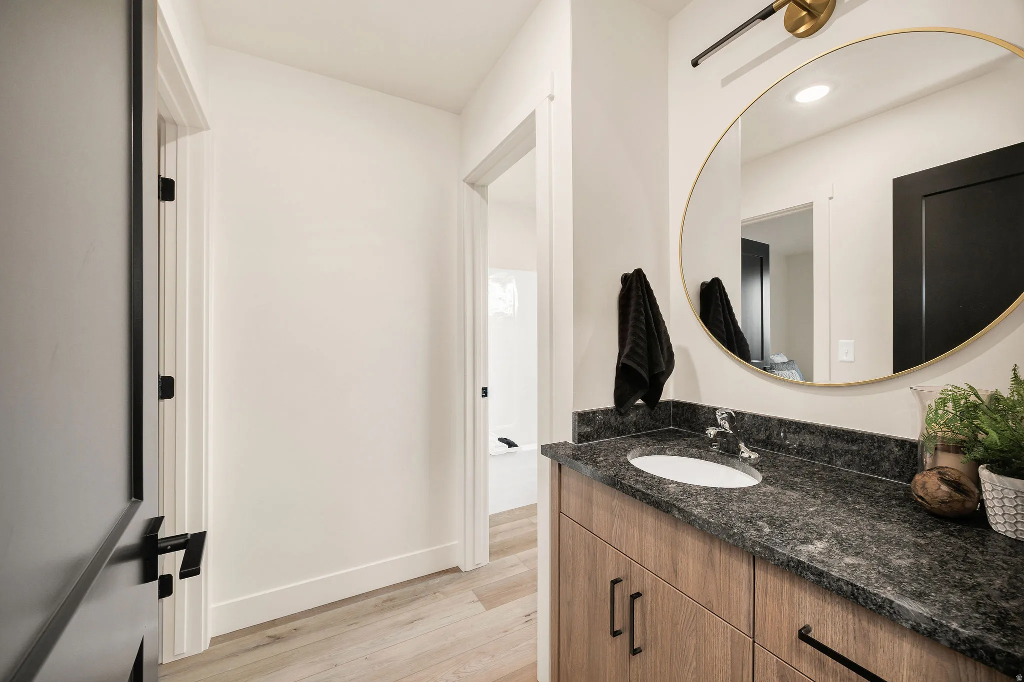 Bathroom vanity featuring a dark granite countertop, undermount sink, and wood-finish cabinetry with matte black hardware