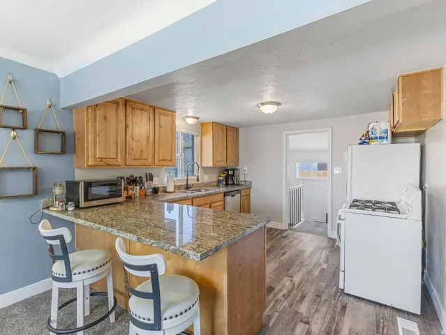 Kitchen featuring light wood cabinetry, a peninsula with granite-finish countertop, stainless steel sink, and wood-finish flooring