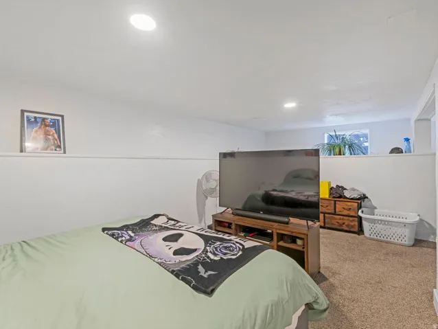Recessed lighting illuminates this room featuring white walls and a light brown carpet