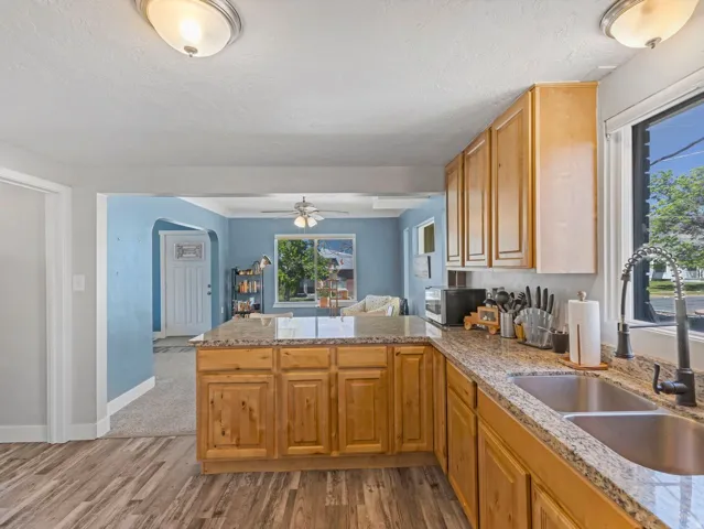 Kitchen featuring wood-finish flooring, natural wood cabinetry, light-toned countertops, a stainless steel double basin sink, and a black pull-down faucet