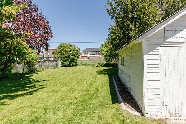 Expansive grass lawn bordered by mature trees and a white-sided outbuilding with a single window
