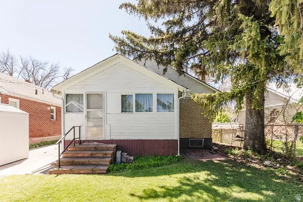 White siding exterior featuring a covered porch entry with brick steps and a black metal handrail