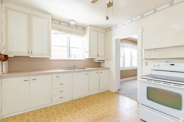 Kitchen featuring white cabinetry with brass-tone hardware, a stainless steel sink, and a white electric range