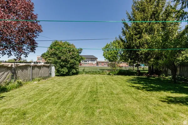 Expansive grass yard with mature trees and a chain-link fence