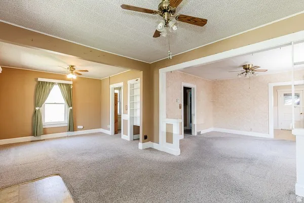 Carpeted living area featuring neutral wall tones, a ceiling fan with integrated lighting, and a double-hung window