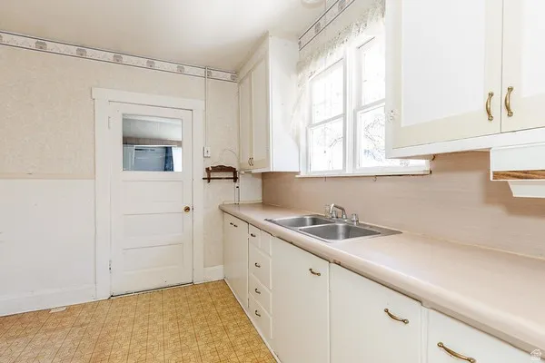 Kitchen featuring white cabinetry with gold-tone hardware, a double-basin stainless steel sink, and a light-toned countertop