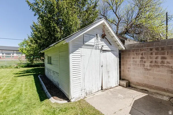 Detached white storage shed featuring a gabled roof, horizontal siding, and double wooden doors