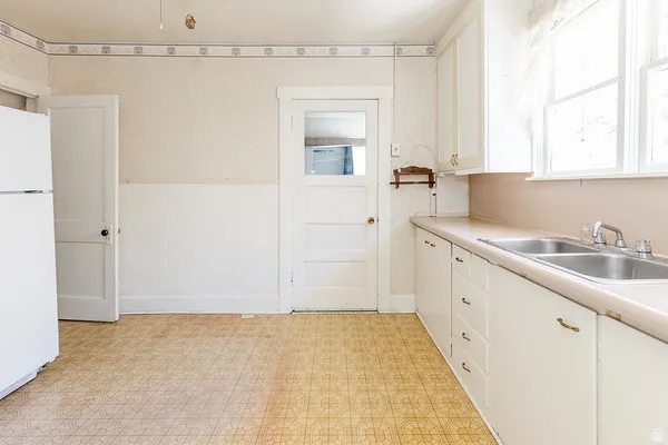 Kitchen area featuring white cabinetry, a double basin stainless steel sink, and light-toned countertops