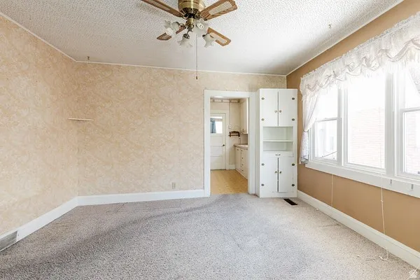 Inviting room featuring a ceiling fan, multiple windows, built-in cabinetry, textured wallpaper, and an entry to an additional space