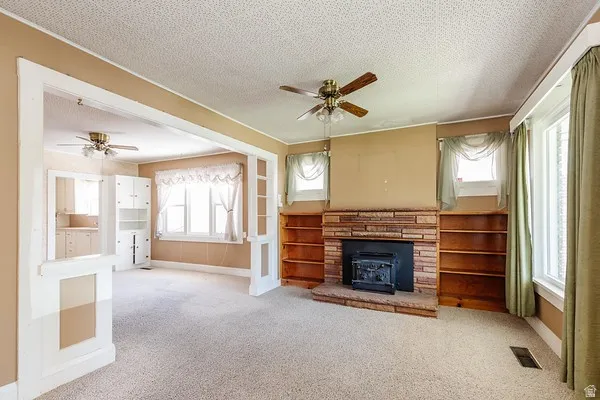 Living area featuring a brick fireplace with a wood-burning stove insert, built-in shelving, and carpet flooring