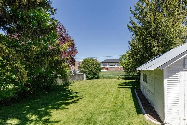 Spacious backyard featuring a manicured lawn, established perimeter trees, and a functional storage shed with a metal roof