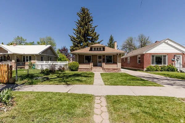 Craftsman-style home featuring a gabled roof, prominent brick porch columns, and a front yard with mature landscaping