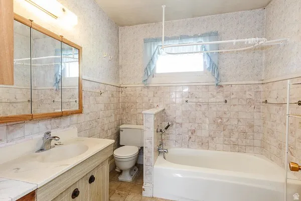 Bathroom featuring a white porcelain bathtub, a toilet, and a vanity with an integrated sink and wood-finish cabinetry