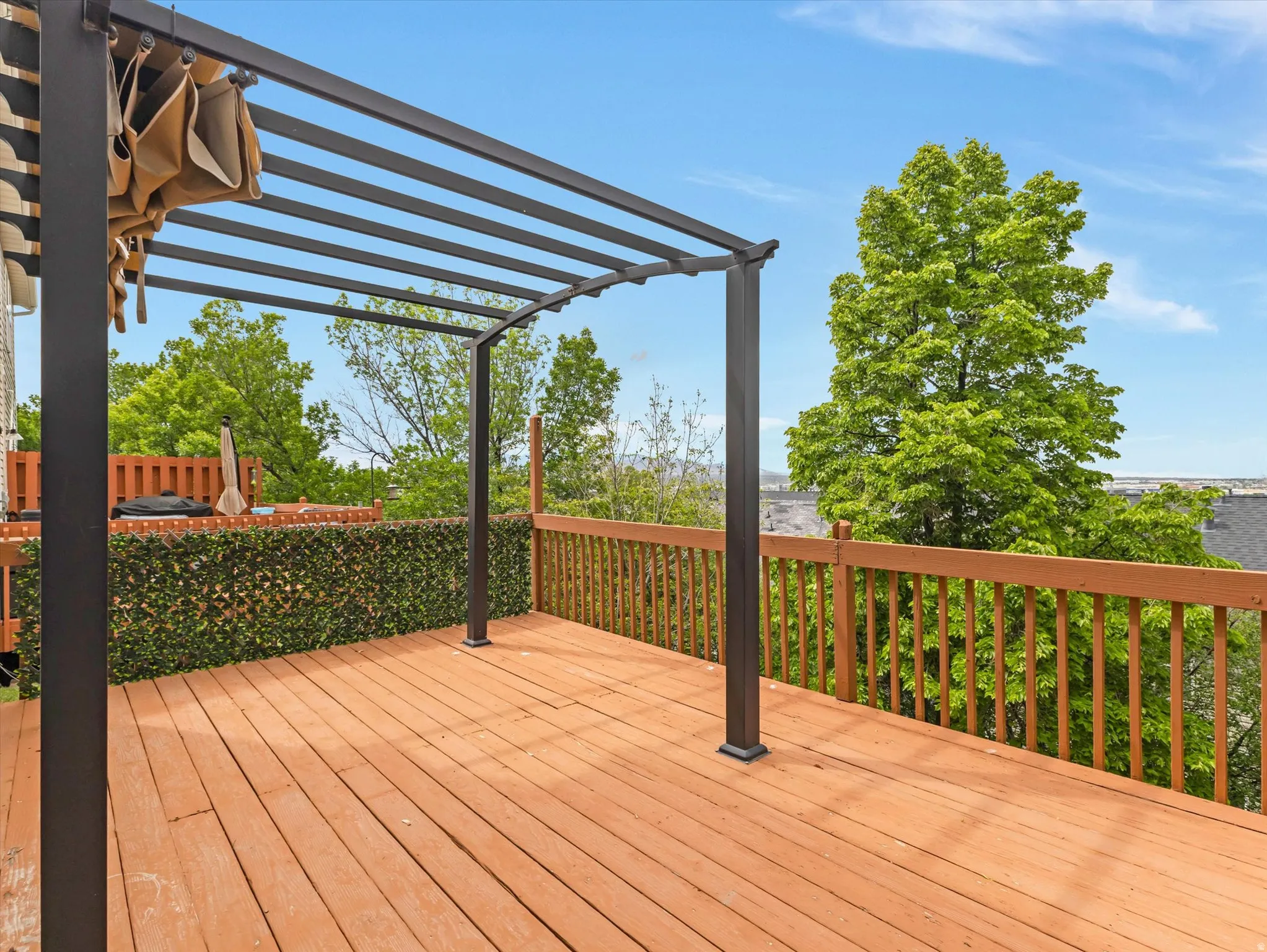Outdoor deck featuring wood-finish flooring and a black metal pergola with a retractable shade