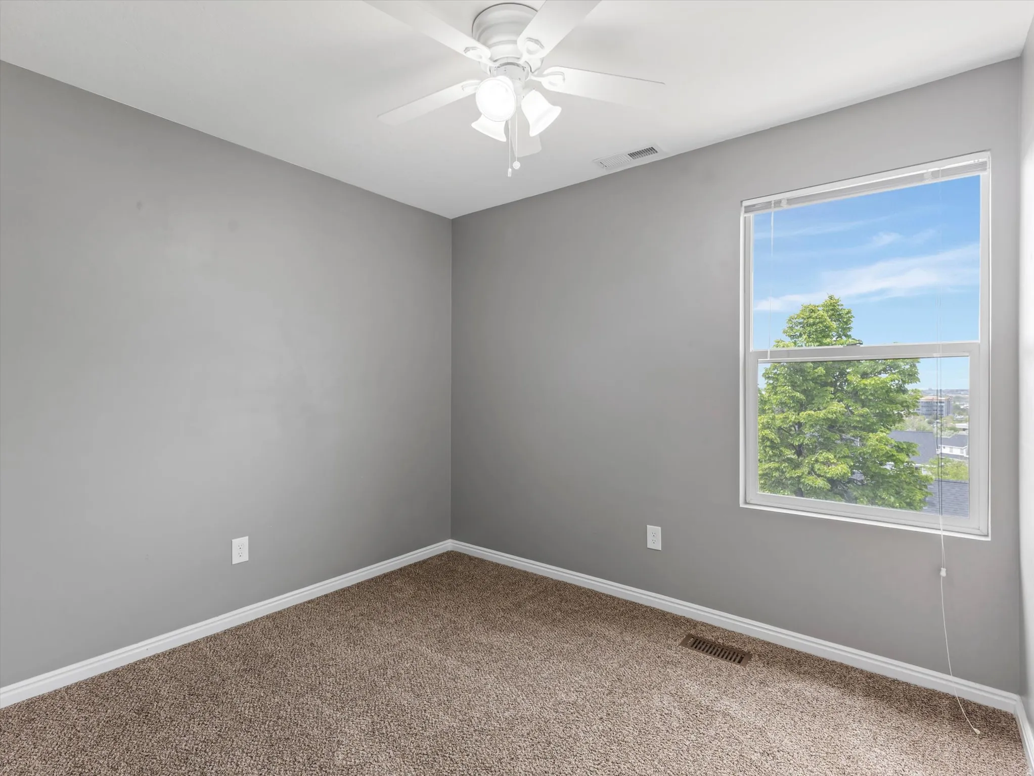 Carpeted room featuring a white ceiling fan with integrated lighting, a single window, and light grey walls with white trim