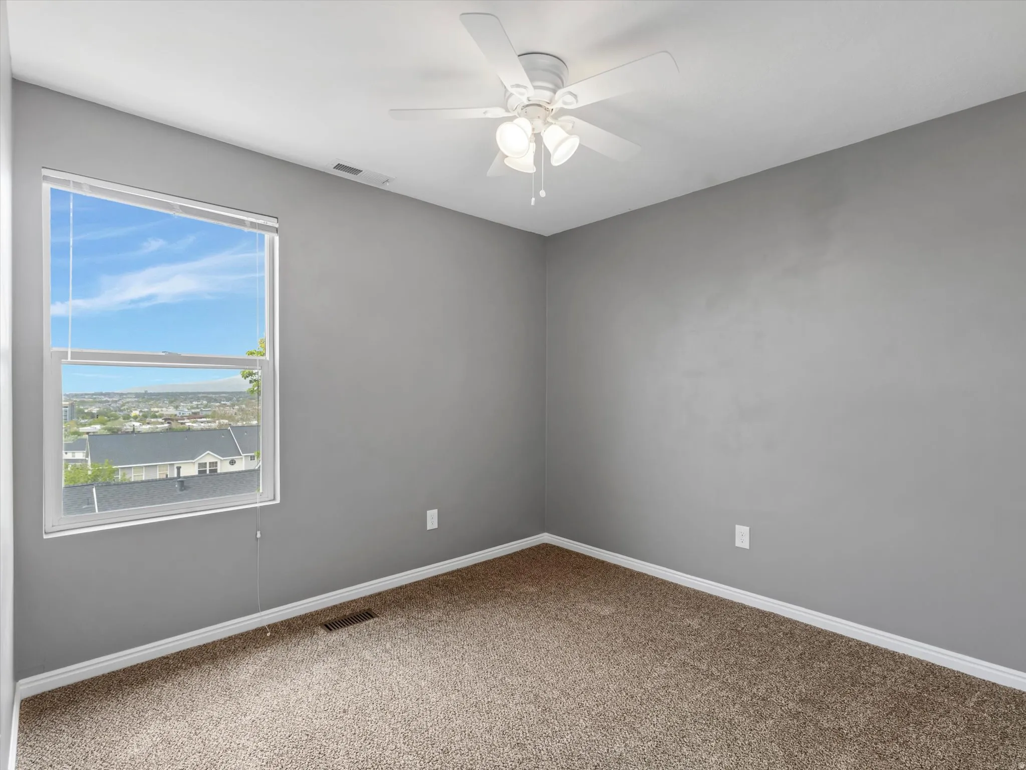 Carpeted room featuring a single window, white trim, a ceiling fan with light fixture, and neutral gray walls