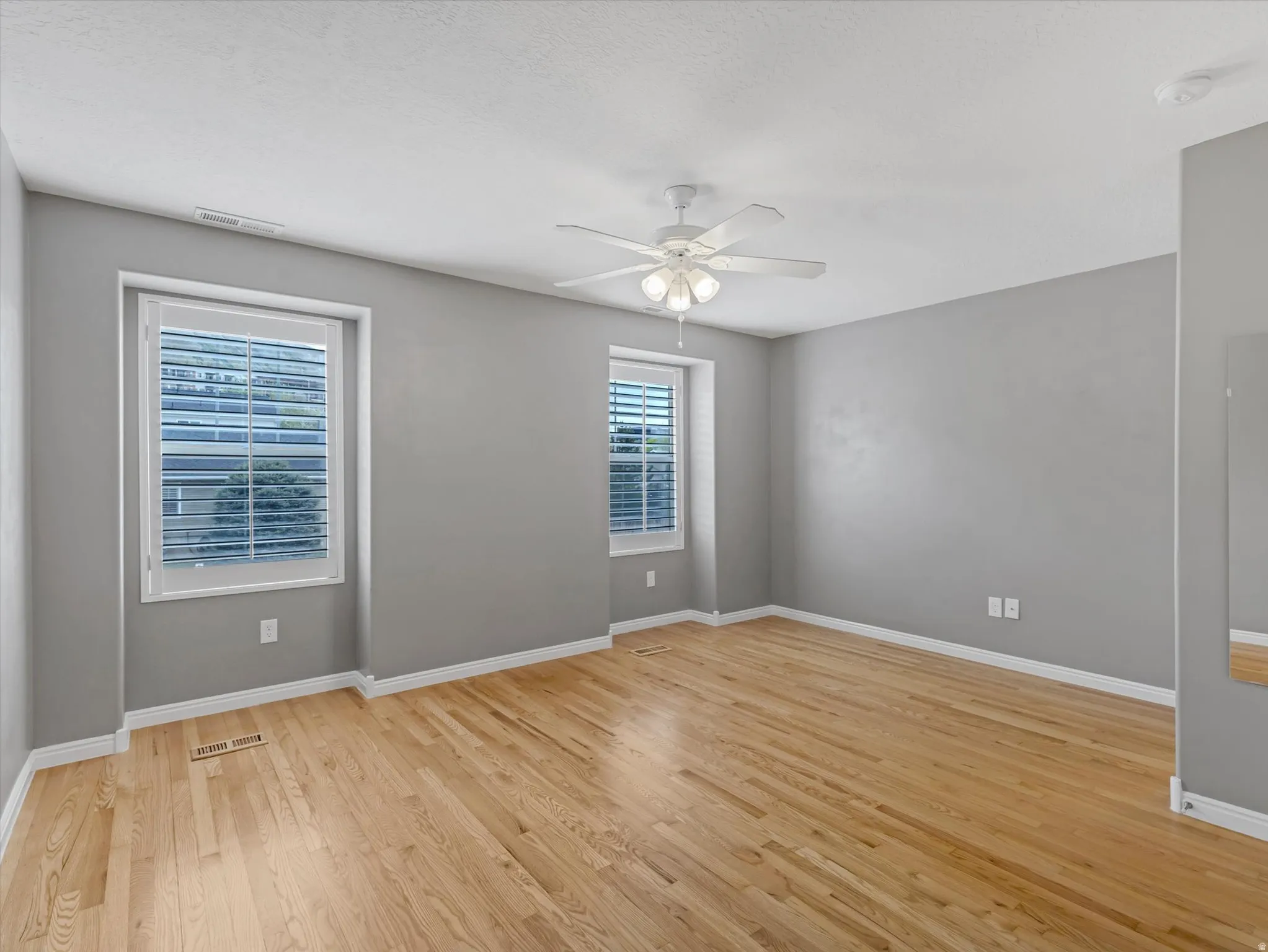 Spacious room with wood-finish flooring, two windows with white blinds, and a ceiling fan with integrated lighting